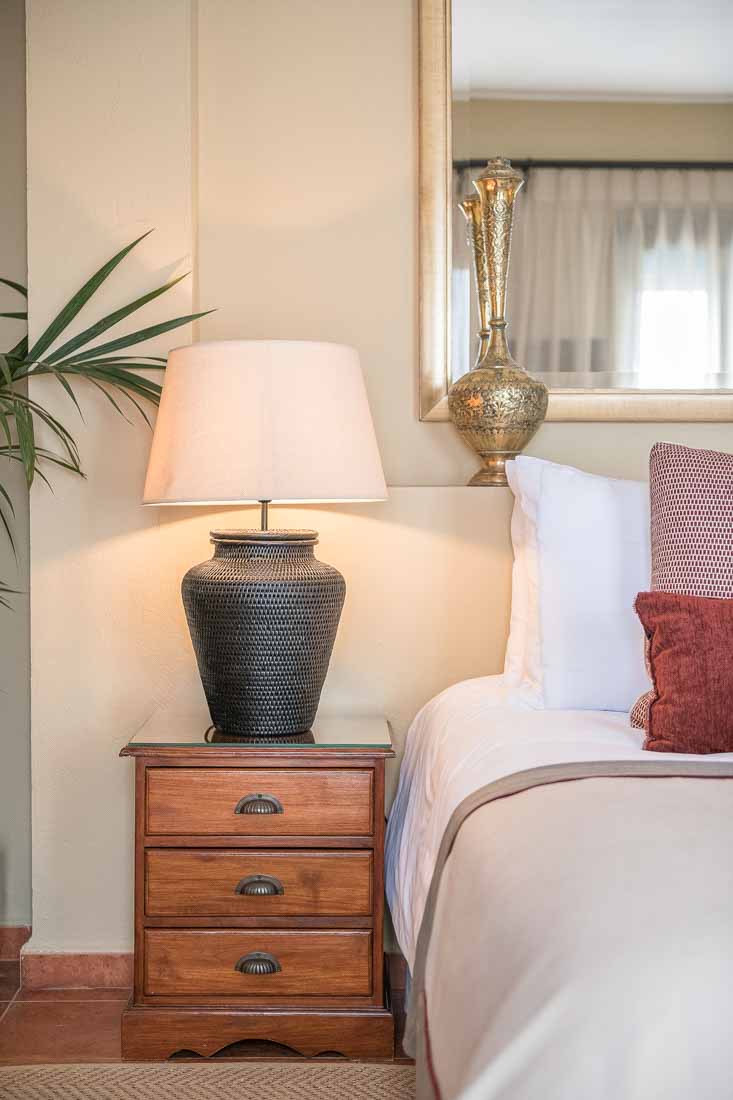 Detalle de la mesilla de noche, lámpara y cama de habitación de hotel